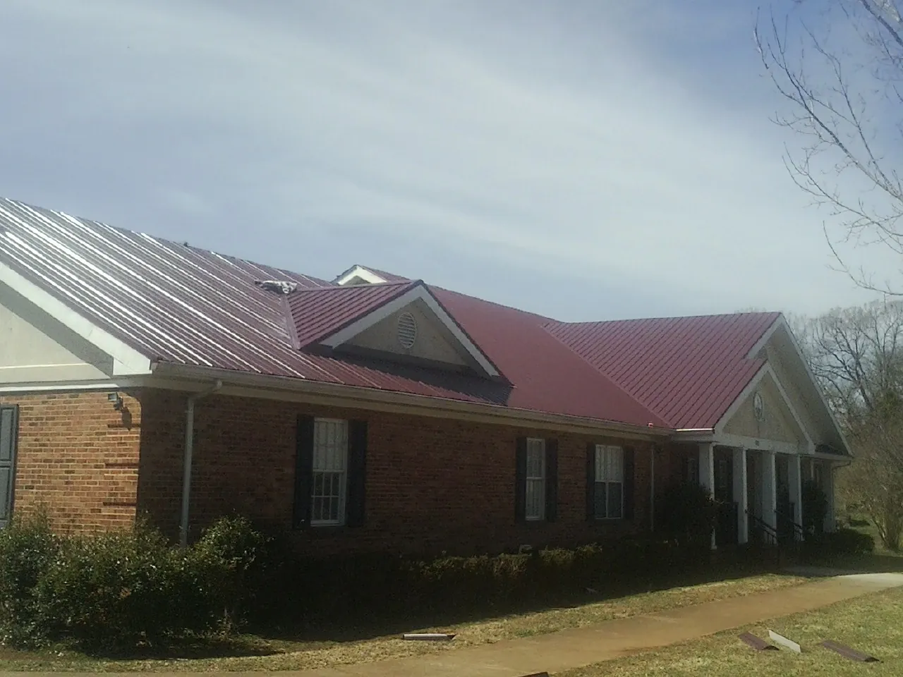 Red metal roof with gabled entries on a long brick building, from a Hail Damage Roof Repair job in Cheshire